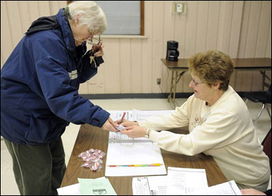 Voter Margaret Henze (left) hands her identification to election inspector Judy Wise on Feb. 21 for a school board primary election in Racine. (AP Photo/Journal Times, Scott Anderson)