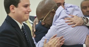 Jonathan Fleming, hugs his attorney Anthony Mayol while his other attorney Taylor Koss applaud in Brooklyn's Supreme court, after a judge declared him a free man on Tuesday April 8, 2014 in New York. Fleming, who spent almost a quarter-century behind bars for murder, was cleared of a killing that happened when he was 1,100 miles away on a Disney World vacation in 1989. (AP Photo/Bebeto Matthews)