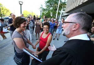 Mel Freitag, left, and Amber Sowards, of Madison, Wis., get married by Daniel Floeter, family court commissioner, outside the City-County Building on Friday, June 6, 2014, in Madison after a federal judge struck down the state's ban on same-sex marriage. Sowards, who is six months pregnant, has been with Freitag for six years. (AP Photo/Wisconsin State Journal, Amber Arnold)