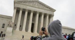 a Supreme Court visitor using his cellphone to take a photo of the court in Washington. A unanimous Supreme Court says police may not generally search the cellphones of people they arrest without first getting search warrants. The justices say cellphones are powerful devices unlike anything else police may find on someone they arrest. (AP Photo, File)