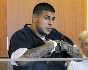 former New England Patriots NFL football player Aaron Hernandez stands during a bail hearing in Superior Court in Fall River, Mass. Hernandez is accused of three murders in Massachusetts. Investigators have appealed for information from tattoo artists who inked his right forearm, but won't say which of Hernandez’s many tattoos prompted their appeal. (AP Photo/Boston Herald, Ted Fitzgerald, Pool, File)
