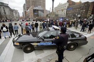 Cleveland police watch demonstrators block Public Square in the city during a protest over the weekend police shooting of 12-year-old Tamir Rice. In cities and states nationwide, police departments are already altering policies and procedures to temper concerns about police conduct in the aftermath of recent cases of black males dying at the hands of white officers. (AP Photo/Mark Duncan, File)