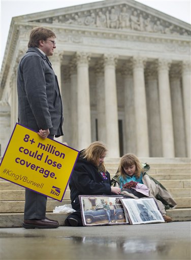 L. Ray Roberts, left stands with his daughters Helena Roberts, 11, center, and her sister Cassie Boyle, 8, right, all from Pittsburgh, on the steps of the Supreme Court in Washington, Wednesday, March 4, 2015, as the court hears arguments in King v. Burwell, a major test of President Barack Obama's health overhaul which, if successful, could halt health care premium subsidies in all the states where the federal government runs the insurance marketplaces. The sisters are holding pictures of their grandmother Hannah Brown, who died when she was 58 years old. Their grandmother lost her job and healthcare and died a year and half later because of lack of access to treatment. (AP Photo/Pablo Martinez Monsivais)