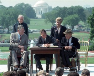 In this July 26, 1990 file photo, President George H. W. Bush signs the Americans with Disabilities Act during a ceremony on the South Lawn of the White House. Joining the president are, from left, Evan Kemp, chairman of the Equal Opportunity Employment Commission; Rev. Harold Wilke; Sandra Parrino, chairman of the National Council on Disability, and Justin Dart, chairman of The President's Council on Disabilities. The Jefferson Memorial is in the background. (AP Photo/Barry Thumma)