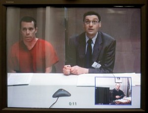 Daniel Shilts Jr., left, the man arrested for explosives at his Waldo, Wis., home last month, sits next to his attorney during his initial appearance via teleconference in Sheboygan, Wis., Tuesday, March 29, 2016. Shilts was charged Tuesday, facing 51 counts of possession of improvised explosives and one count of possession of explosive materials to make an improvised device, all felonies. (Gary C. Klein/The Sheboygan Press via AP)