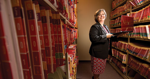 Flanked by older case files, Ozaukee County's Clerk of Circuit Court Mary Lou Mueller holds a laptop while in the clerk’s office on July 14 at the Ozaukee County Justice Center. (File photo by Kevin Harnack)