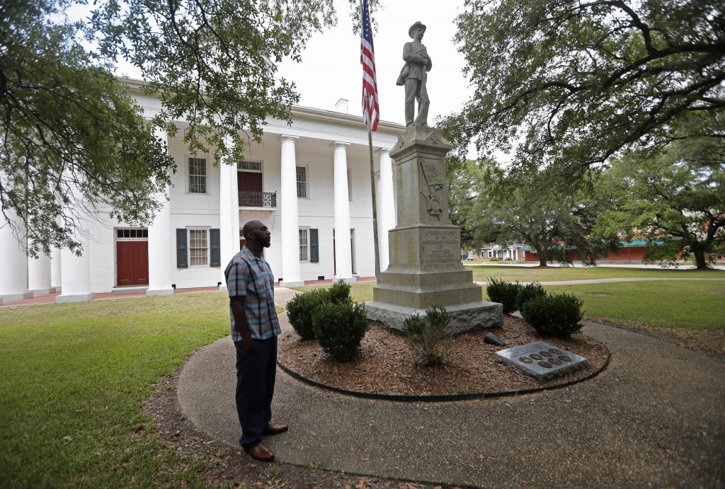 In this Aug. 1, 2018 photo, Ronnie Anderson, an African-American man charged with possession of a firearm by a convicted felon, waits next to a confederate statue on the lawn of the East Feliciana Parish Courthouse in Clinton, La. Anderson is asking for his case to be moved to another location because the courthouse where he's being tried has a Confederate monument in front of it. (AP Photo/Gerald Herbert)