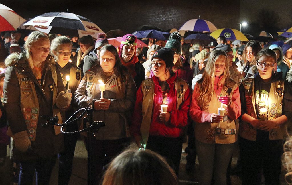 Girl Scouts sing as hundreds of community members turn out in the rain Sunday evening, Nov. 4, 2018, for a candlelight vigil at Halmstad Elementary School in Chippewa Falls, Wis., in remembrance of three fourth grade Girl Scouts and a parent who died Saturday, after being struck by a pickup truck while their troop was picking up trash along a rural highway. The 21-year-old driver, Colten Treu of Chippewa Falls, sped off but later surrendered. He will be charged with four counts of homicide, Lake Hallie police Sgt. Daniel Sokup said. (Steve Kinderman/The Eau Claire Leader-Telegram via AP)