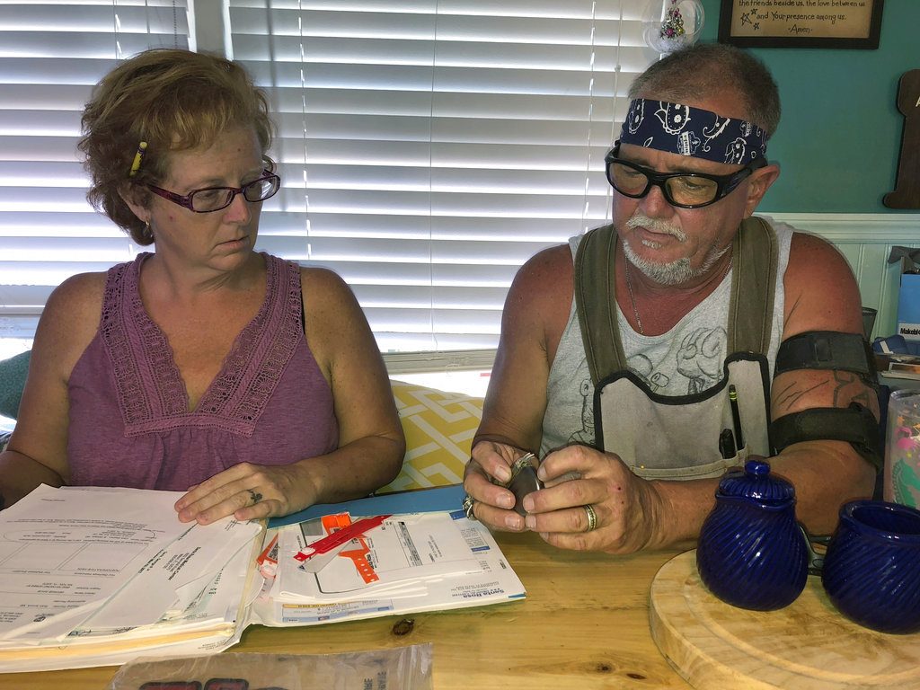 In this Oct. 31 2018 photo, George and Brenda Davis look at his nerve stimulator and medical documents at their home in Milton, Fla. George Davis had three Medtronic spinal-cord implants between 2003 and 2007 after a car accident mangled his back. They temporarily reduced some of his pain, but he said the non-rechargeable batteries that were supposed to last for years never did and he tired of multiple surgical removals. In 2015, he decided to try a Boston Scientific device. But he said he soon started feeling pain shooting down his back and legs and a burning sensation at the implant site. Brenda Davis said Boston Scientific disregarded her complaints after her husband suffered a life-threatening infection following implant surgery. (AP Photo/Holbrook Mohr)
