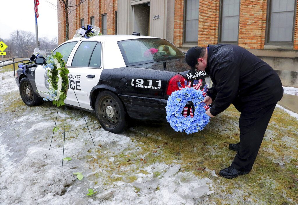 Timothy Nelson, of Oak Creek, Wis., places small flags in a bouquet near a squad car adorned with flowers as a memorial for fallen Milwaukee Police Officer Matthew Rittner at the Neighborhood Task Force police building in Milwaukee on Thursday, Feb. 7, 2019.  Police are collecting evidence at a Milwaukee home where a police officer was fatally shot while serving a warrant. Investigators say 35-year-old Officer Matthew Rittner was killed Wednesday as members of Milwaukee's Tactical Enforcement Unit served the warrant on someone suspected of illegally selling firearms and drugs. (Mike De Sisti/Milwaukee Journal-Sentinel via AP)