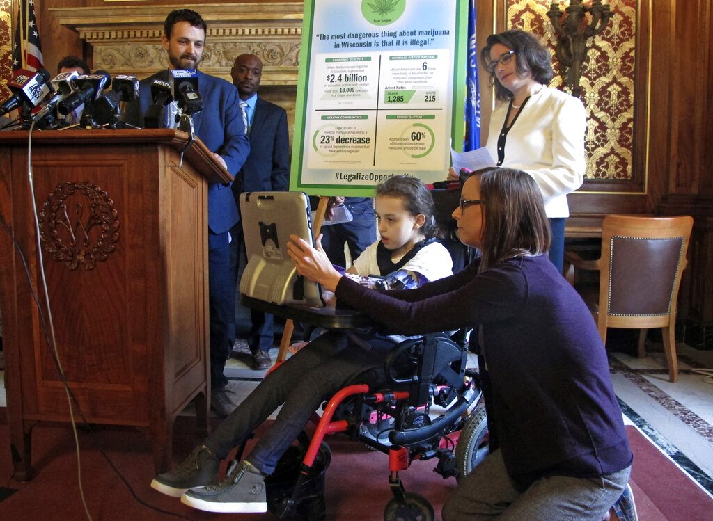 Norah Lowe, 10, speaks through a computer in favor of legalizing medical marijuana with her mother, Megan, at her side while her dad, Josh, stands at the podium and state Rep. Melissa Sargent watches on Thursday, April 18, 2019, in Madison, Wisc. The Lowes and others attended a news conference announcing Sargent's latest attempt in the Wisconsin Legislature to legalize marijuana. (AP Photo/Scott Bauer)