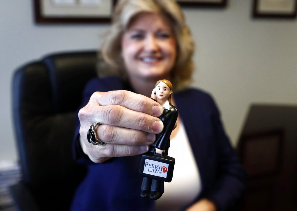 In this Tuesday, May 14, 2019, photo, business owner Meloney Perry, of Perry Law, shows off her miniature Meloney Perry Stress Doll as she poses for a portrait at her law firm in Dallas. Perry once worked at a traditional big law firm with a formal, corporate atmosphere, and knew she wanted a different culture at her own firm. “I learned the ‘old school’ way, but it’s changed,” says Perry. “Nowadays, with the employees coming in younger, you do have to have more of a family feel.” (AP Photo/Tony Gutierrez)