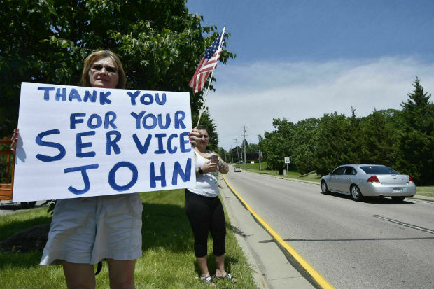 Karen Giannola, left, holds a sign during a procession for the Racine officer John Hetland following his funeral at Carthage College in Kenosha,on Wednesday. (Sean Krajacic/The Kenosha News via AP)