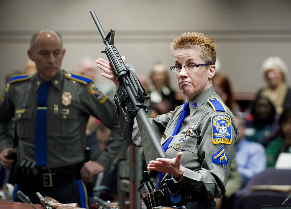 FILE - In this Jan. 28, 2013, file photo, firearms training unit Detective Barbara J. Mattson, of the Connecticut State Police, holds up a Bushmaster AR-15 rifle, the same make and model of gun used by Adam Lanza in the December 2012 Sandy Hook School shooting, during a hearing of a legislative subcommittee in Hartford, Conn. Gunmaker Remington Arms filed a request on Thursday, Aug. 1, 2019, asking the U.S. Supreme Court to hear its appeal of a Connecticut court ruling that reinstated a wrongful death lawsuit against the company. Remington cited a 2005 federal law that shields gunmakers in most cases from liability when their products are used in crimes. (AP Photo/Jessica Hill, File)