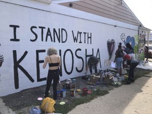 Volunteers paint murals on boarded-up businesses in Kenosha on Sunday at an "Uptown Revival." The event was meant to gather donations for Kenosha residents and help businesses hurt by violent protests that sparked fires across the city following the police shooting of Jacob Blake. (AP Photo/ Russell Contreras)