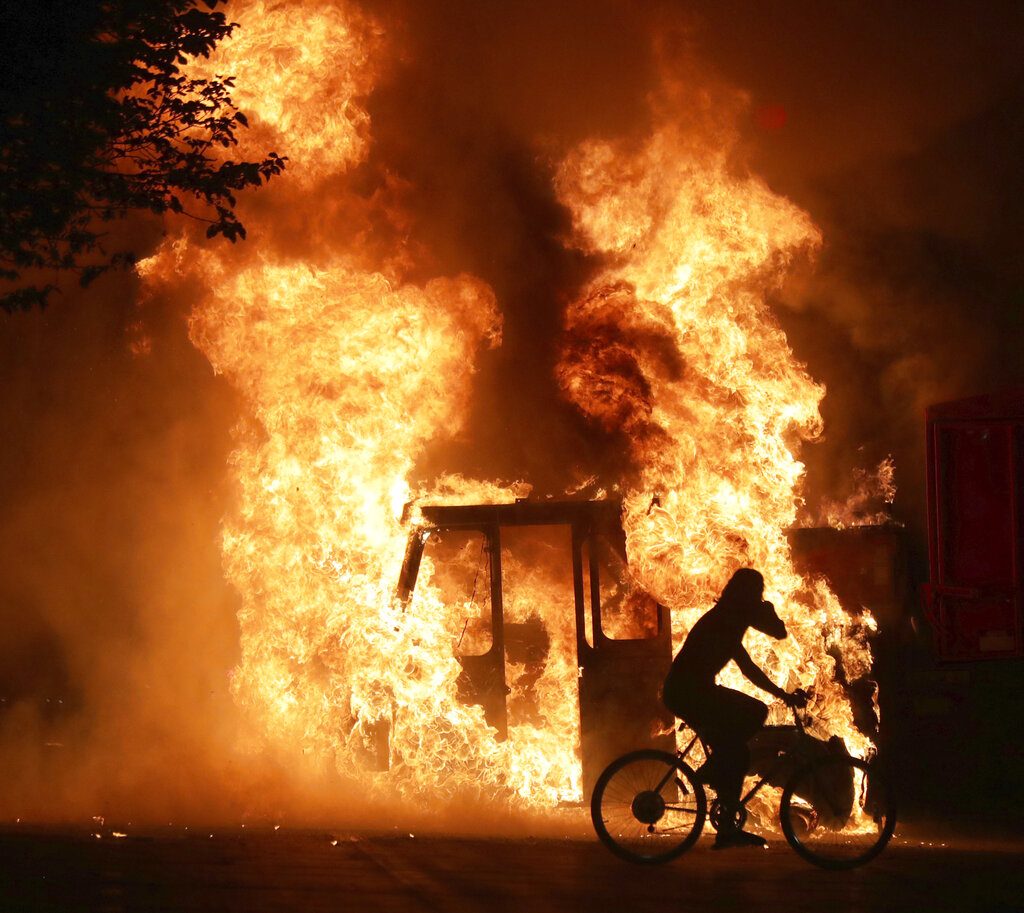 A man on a bike rides past a city truck on fire outside the Kenosha County Courthouse in Kenosha, Wis., on Sunday, Aug. 23, 2020. Kenosha police shot a man Sunday evening, setting off unrest in the city after a video appeared to show the officer firing several shots at close range into the man's back. (Mike De Sisti/Milwaukee Journal-Sentinel via AP)
