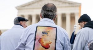 A man wears a sign on his back that reads "Unborn Lives Matter" as he and other anti-abortion protesters wearing doctors uniforms demonstrate in front of the U.S. Supreme Court on Wednesday in Washington as the court hears arguments in a case from Mississippi, where a 2018 law would ban abortions after 15 weeks of pregnancy, well before viability. (AP Photo/Andrew Harnik)