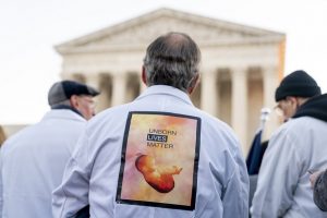 A man wears a sign on his back that reads "Unborn Lives Matter" as he and other anti-abortion protesters wearing doctors uniforms demonstrate in front of the U.S. Supreme Court on Wednesday in Washington as the court hears arguments in a case from Mississippi, where a 2018 law would ban abortions after 15 weeks of pregnancy, well before viability. (AP Photo/Andrew Harnik)